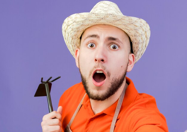 Un jardinier choqué portant un chapeau de jardinage tient un râteau à houe