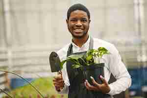 Photo gratuite jardinier dans un tablier. guy africain dans une serre. fleurs dans un pot.