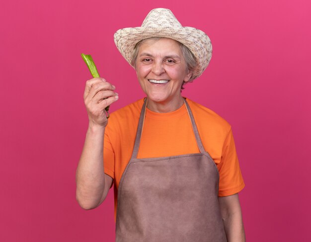 Jardinier femme âgée souriante portant un chapeau de jardinage tenant du piment cassé