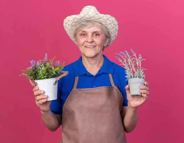 Jardinier femme âgée souriante portant un chapeau de jardinage tenant des pots de fleurs