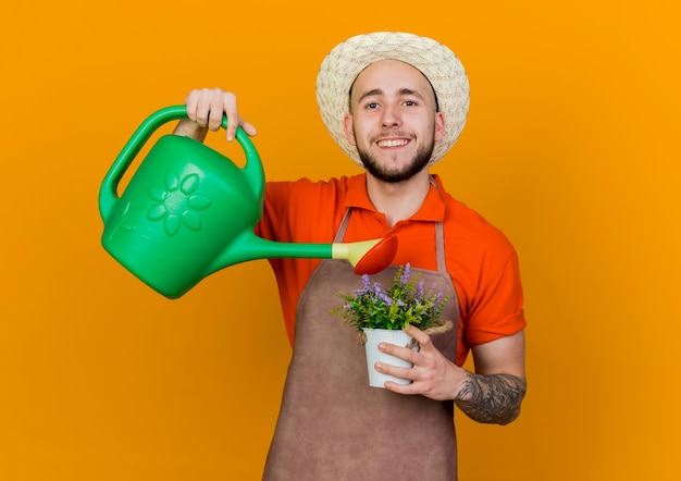 Jardinier mâle souriant portant chapeau de jardinage détient arrosoir peut faire semblant d'arroser les fleurs en pot