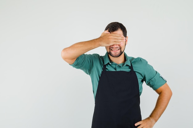 Jardinier masculin couvrant les yeux avec la main en t-shirt, tablier et l'air excité. vue de face.