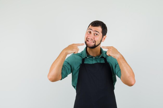 Jardinier masculin en t-shirt, tablier pointant sur ses dents, vue de face.