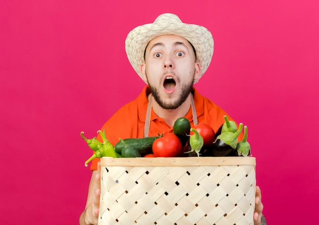 Photo gratuite un jardinier surpris portant un chapeau de jardinage tient un panier de légumes