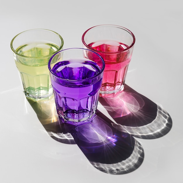 Jaune; boisson rose et violette dans des verres avec une ombre sur fond blanc