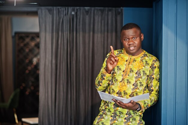 Je l'ai choisi Homme afro amical en vêtements jaunes traditionnels au restaurant tenant le menu à portée de main et choisit les plats