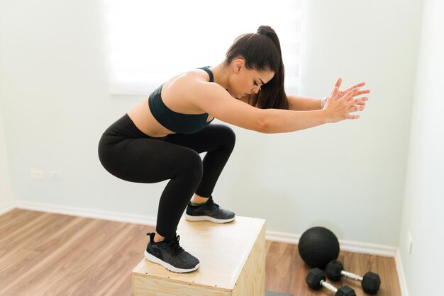 Je l'ai fait. Jolie femme sautant et faisant des squats sur une plyo box pour son entraînement cardio et son entraînement croisé