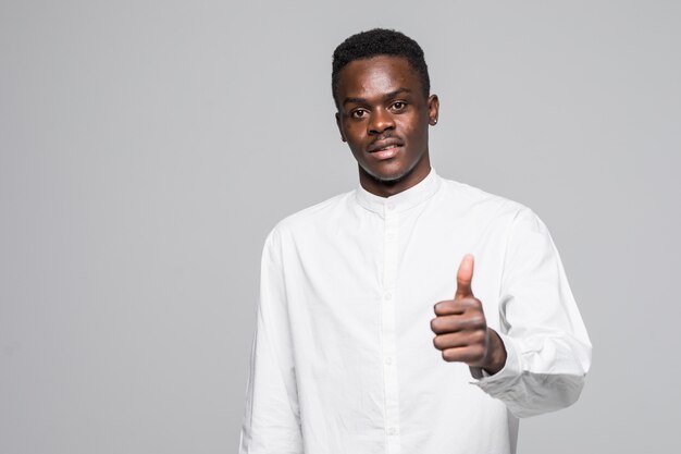 Je l'aime. Jeune étudiant universitaire masculin attrayant avec une coiffure afro en t-shirt blanc décontracté souriant, montrant le pouce vers le haut à huis clos avec une expression heureuse et excitée