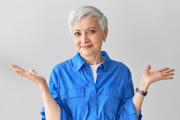 Photo gratuite je n'ai aucune idée. élégante femme d'âge mûr émotionnelle avec de courts cheveux gris exprimant la confusion, haussant les épaules, perplexe et perdue, disant que je ne sais pas. le langage du corps