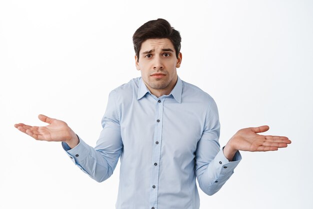 Je ne sais pas. Homme d'entreprise ignorant, employé de bureau haussant les épaules et ayant l'air confus, debout perplexe contre le mur blanc