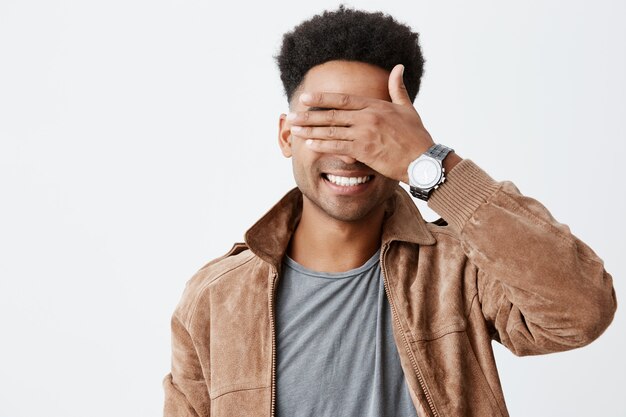 Je ne te vois pas. Close up portrait of young attractive dark skinned man with afro hairstyle in casual autumn siling, closed eyes with hand, playing with little child on street.