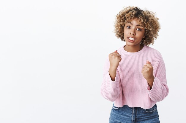 Je te jure de te tuer. Portrait d'une femme afro-américaine énervée et énervée avec une coupe de cheveux blonde levant les poings serrés et serrant les dents dans un combat de cueillette d'indignation agressif sur un mur blanc