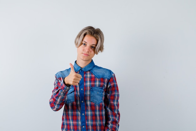 Jeune adolescent en chemise à carreaux montrant le pouce vers le haut et l'air heureux, vue de face.