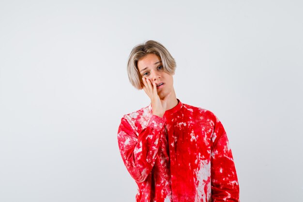 Jeune adolescent en chemise avec la main près de la bouche et l'air désespéré, vue de face.