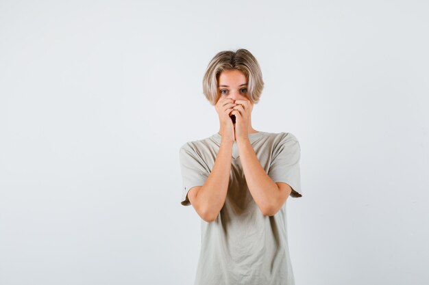 Jeune adolescent gardant les mains sur la bouche en t-shirt et ayant l'air effrayé. vue de face.