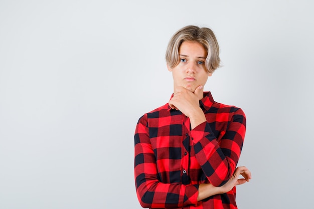 Photo gratuite jeune adolescent avec la main sur le menton en chemise à carreaux et à la colère. vue de face.