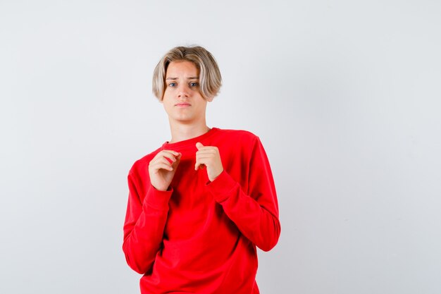 Jeune adolescent avec les mains sur la poitrine en pull rouge et l'air effrayé. vue de face.