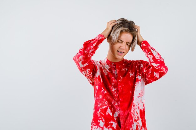 Jeune adolescent avec les mains sur la tête, fermant les yeux en chemise et ayant l'air oublieux. vue de face.