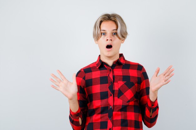 Jeune adolescent montrant un geste d'abandon en chemise à carreaux et ayant l'air effrayé, vue de face.