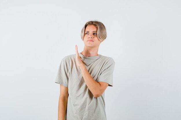 Jeune adolescent montrant un geste d'arrêt tout en détournant les yeux en t-shirt et ayant l'air effrayé, vue de face.