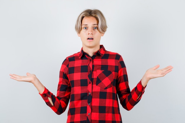 Jeune adolescent montrant un geste impuissant en chemise à carreaux et hésitant. vue de face.