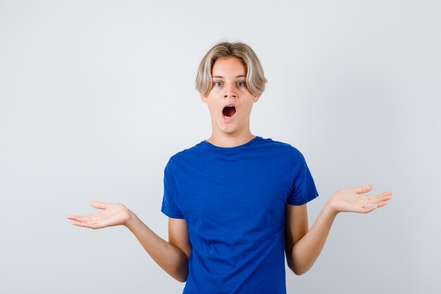 Jeune adolescent montrant un geste impuissant en t-shirt bleu et l'air perplexe, vue de face.