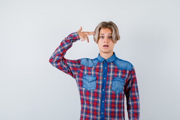 Jeune adolescent montrant un geste de suicide en chemise à carreaux et ayant l'air choqué. vue de face.