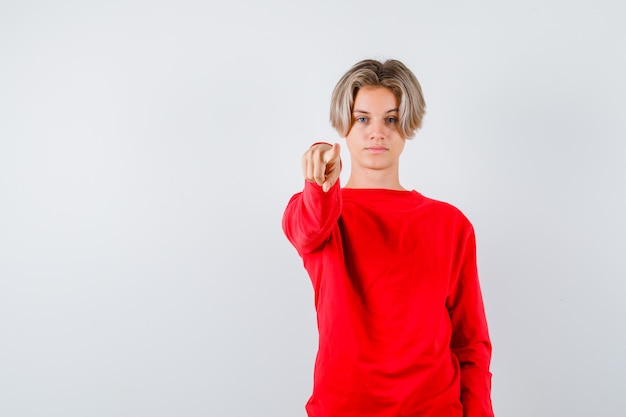 Jeune adolescent pointant vers l'avant en pull rouge et ayant l'air sérieux. vue de face.