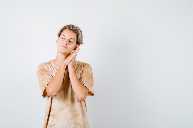 Jeune adolescent s'appuyant sur les paumes comme oreiller en t-shirt et ayant l'air endormi. vue de face.