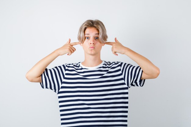 Jeune adolescent se bouchant les oreilles avec les doigts, boudant les lèvres en t-shirt rayé et ayant l'air effrayé. vue de face.