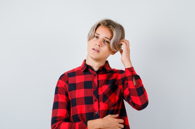 Jeune adolescent se grattant la tête en chemise à carreaux et à la réflexion, vue de face.