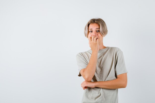 Jeune adolescent se rongeant les ongles avec émotion en t-shirt et ayant l'air anxieux. vue de face.