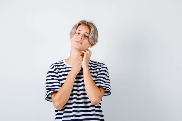 Jeune adolescent touchant le cou avec les mains en t-shirt rayé et ayant l'air en détresse. vue de face.