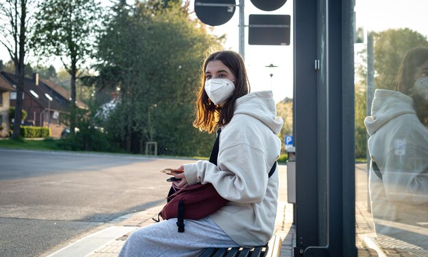 Une jeune adolescente attend un bus à un arrêt de bus tôt le matin