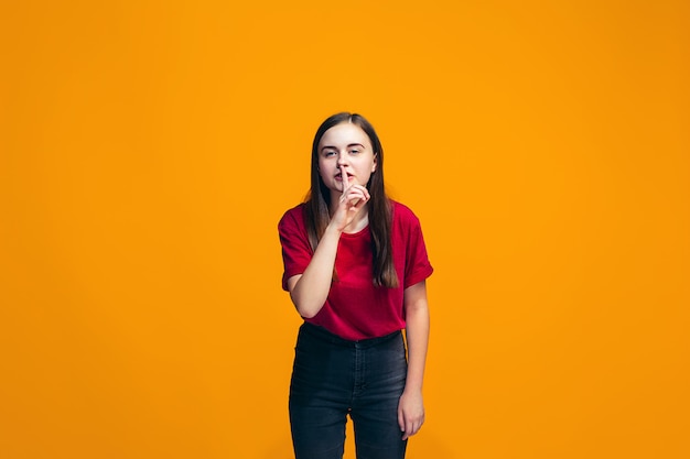 La jeune adolescente chuchotant un secret derrière sa main sur le mur orange