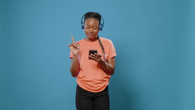 Jeune adulte avec un casque faisant des mouvements de danse et utilisant un smartphone pour changer de chanson. Personne positive écoutant de la musique sur un casque et regardant l'écran du téléphone portable, s'amusant et dansant.