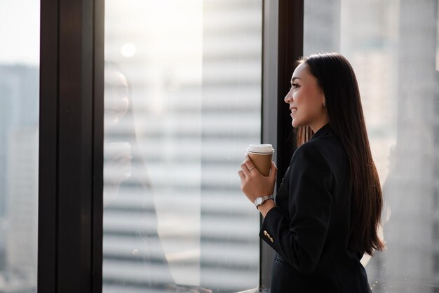 Jeune adulte femme d'affaires asiatique intelligente en costume décontracté noir tenant une tasse de café pendant la pause