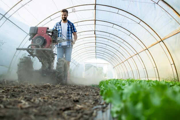 Jeune agriculteur travaillant dur cultivateur à moteur pour préparer le sol pour les nouveaux semis dans la ferme d'aliments biologiques