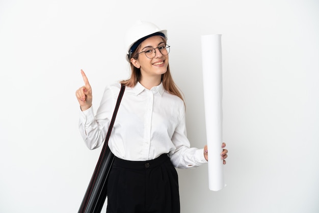 Jeune architecte femme avec casque et tenant des plans isolés sur un mur blanc montrant et en soulevant un doigt en signe du meilleur