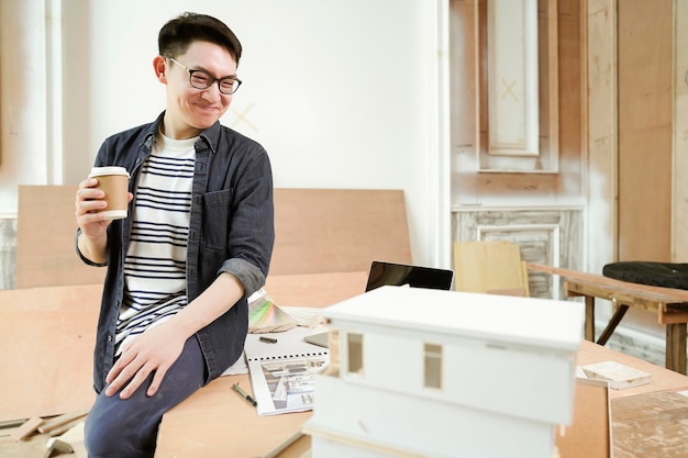 Photo gratuite jeune architecte masculin à lunettes asiatiques attrayant sourire confiant fier de présenter un nouveau projet de modèle de maison bonheur asiatique travaillant avec une étude de modèle de masse du projet de conception de maison