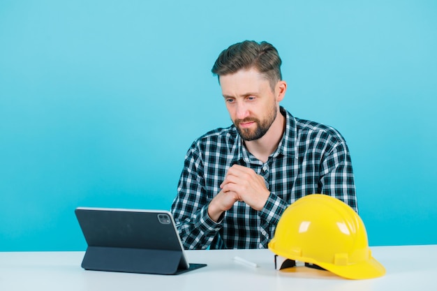 Jeune architecte regarde l'écran de la tablette en tenant les mains sur la poitrine sur fond bleu