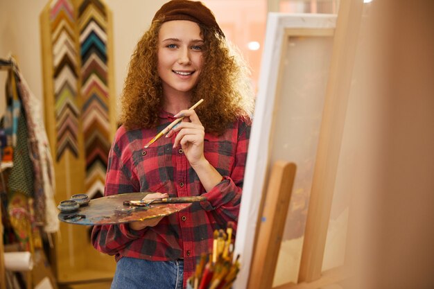 Jeune artiste frisé semble heureux et détient une palette de peintures à l'huile