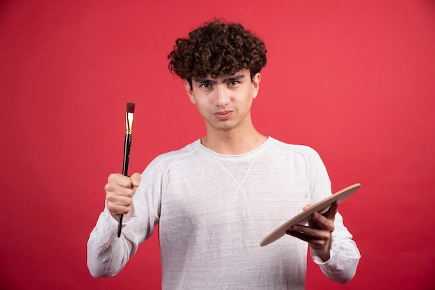 Jeune artiste masculin regardant la caméra avec des outils de peinture.