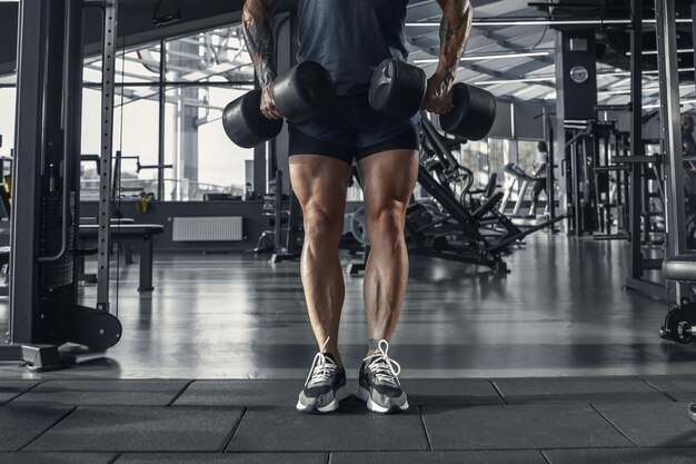 Jeune athlète caucasien musclé pratiquant dans la salle de gym avec les poids.