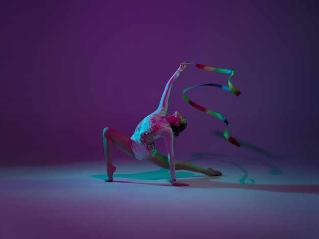 Jeune Athlète Féminine, Artiste De Gymnastique Rythmique Danse, Formation Isolée Sur Fond Violet Studio Avec Néon. Belle Fille Pratiquant Avec Un équipement. Grâce Dans La Performance.