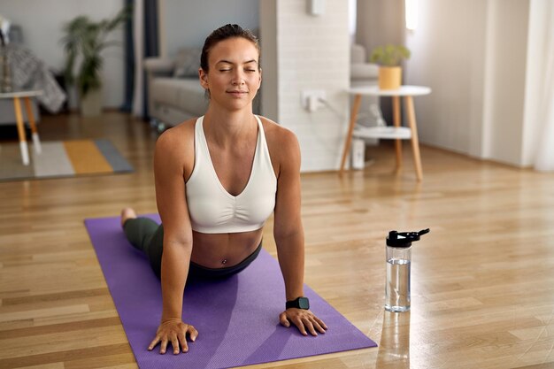 Jeune athlète féminine pratiquant le yoga en cobra pose dans son salon