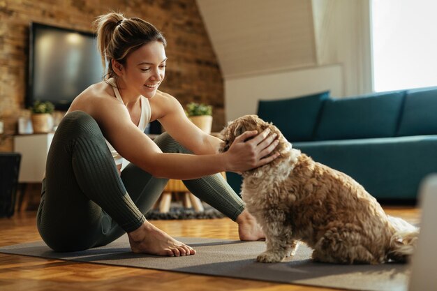 Jeune athlète féminine se relaxant avec son chien sur le sol dans le salon