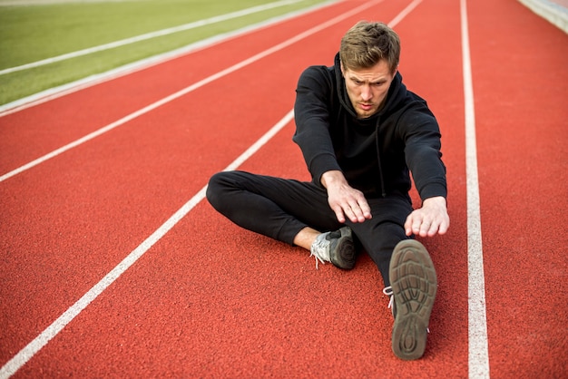 Jeune athlète masculin assis sur la piste de course qui s'étend de la main et des jambes