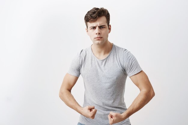 Jeune athlète masculin caucasien avec un corps musclé, démontrant sa force, se vante de lui-même. Un gars positif fronce les sourcils, montre des muscles et de la force, a une expression confiante, prêt à se battre.