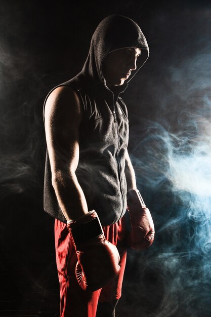Le jeune athlète masculin kickboxing debout sur un fond de fumée bleue